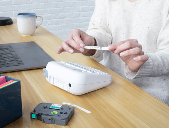 Person using Ptouch PT220 to create labels with label tape cartridge on desk