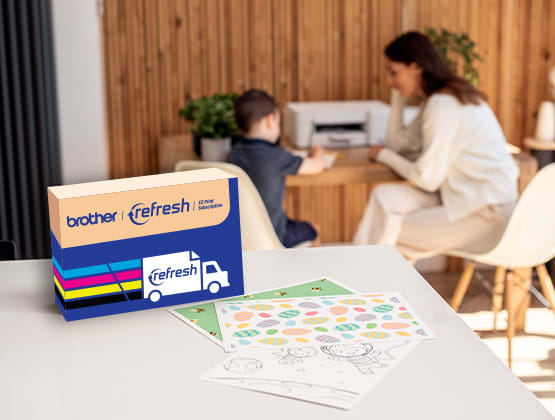 Refresh subscription box on a counter with a woman and child in background sitting at a desk with a Brother printer.