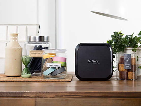 P-touch Cube Plus on a wooden counters with decorative jars and plants.