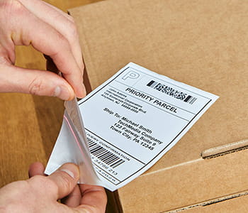 Person peeling shipping label created with QL-1100C label printer and preparing to place on a box. 