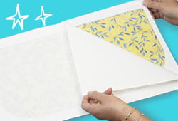 Person removing laminated sheet to reveal blue leaves on yellow background printed fabric