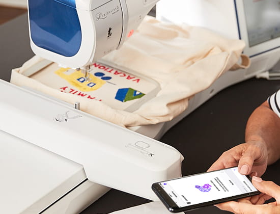 Person using the My Stitch Monitor app on a mobile device with embroidery machine in background with design in the hoop